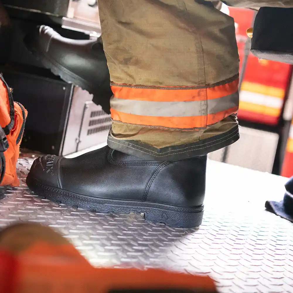 Black Fire Hunter USA NFPA-certified structural boots worn with turnout pants inside of a firetruck with diamond metal plate