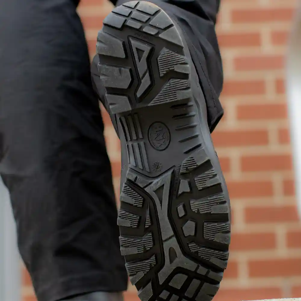 Close up on black rugged tread of Enforce X High Winter insulated boots with red brick wall in the background.